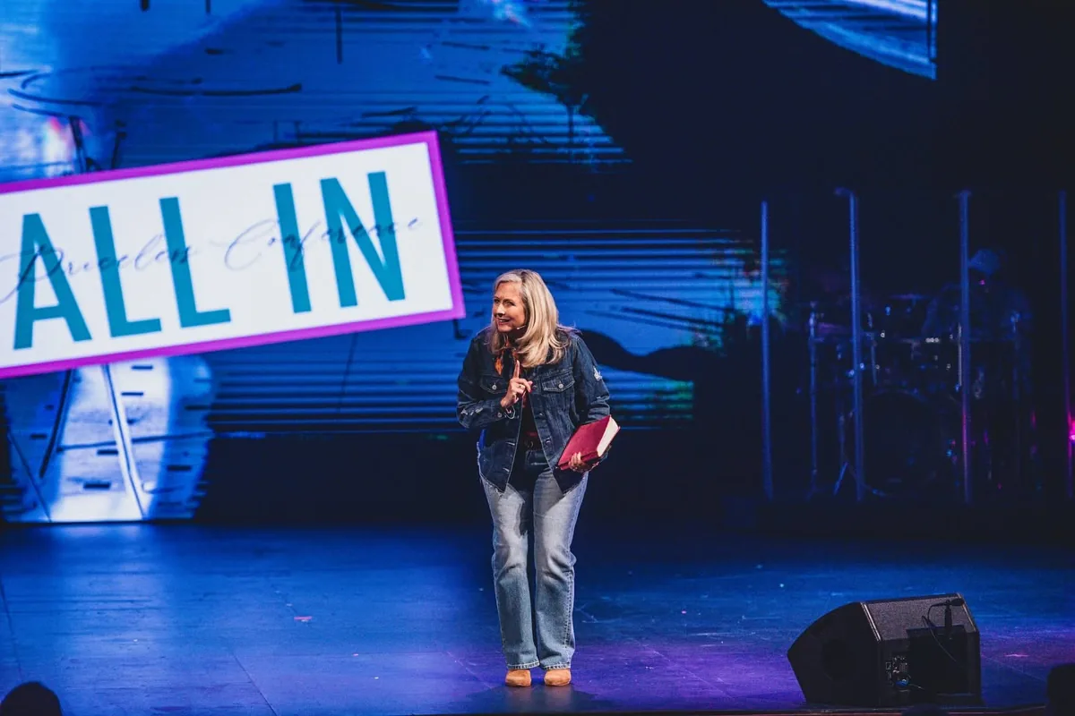 Kim Kjos speaking beside the All In sign at Priceless 2025