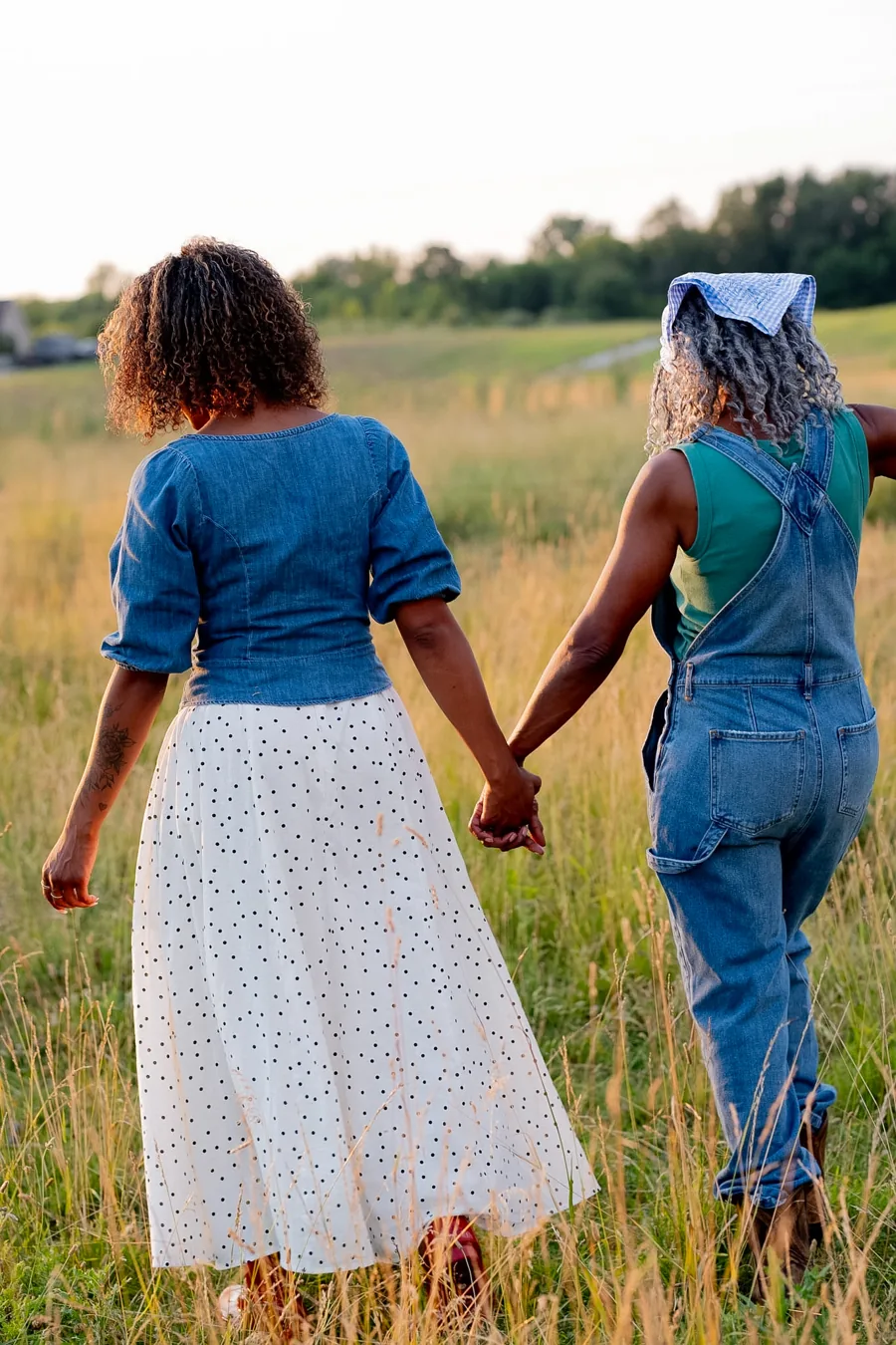 Two women walking hand in hand through the field in the 2027 photoshoot