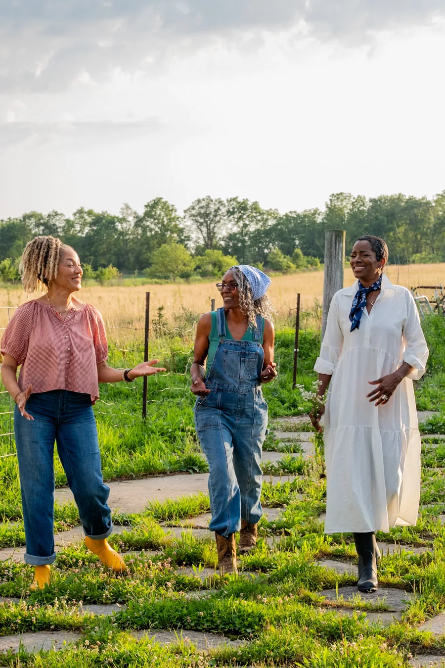 Three women walking and talking beside a sunlit field in the 2027 photoshoot